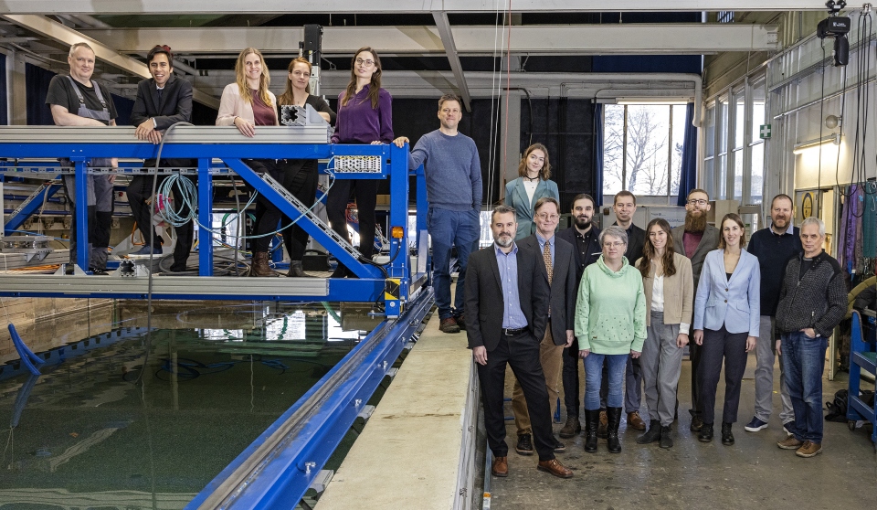 Das Team des Lehrstuhls Strömungsmechanik steht am Schleppkanal und auf dem Schleppwagen in der Strömungshalle.